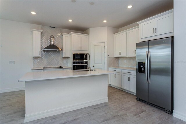 kitchen featuring tasteful backsplash, black appliances, wall chimney exhaust hood, white cabinets, and a kitchen island with sink