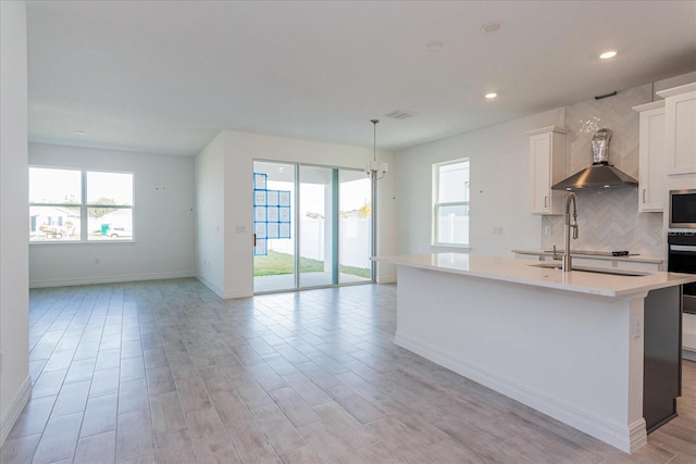 kitchen with wall chimney range hood, white cabinetry, a kitchen island with sink, and light hardwood / wood-style floors