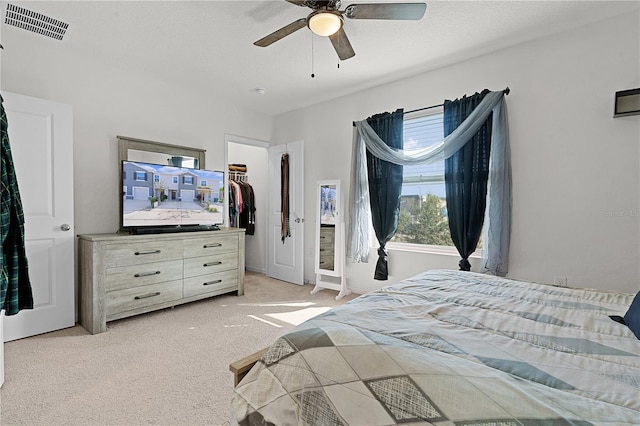 bedroom featuring a walk in closet, ceiling fan, a textured ceiling, a closet, and light colored carpet