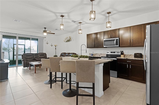 kitchen with appliances with stainless steel finishes, sink, hanging light fixtures, a breakfast bar area, and a kitchen island with sink