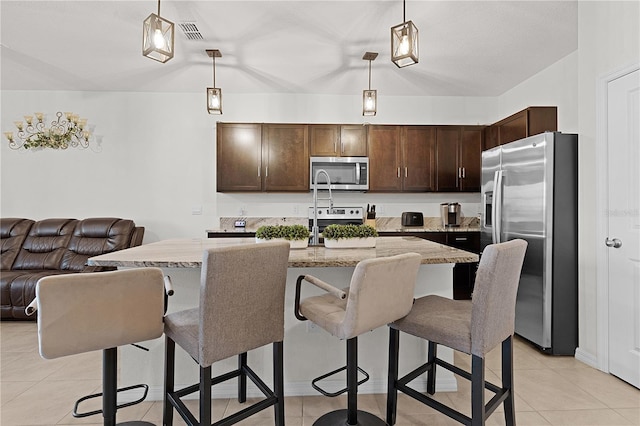 kitchen featuring a breakfast bar, appliances with stainless steel finishes, decorative light fixtures, and a center island with sink