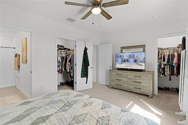 bedroom with a walk in closet, light carpet, ensuite bathroom, and ceiling fan