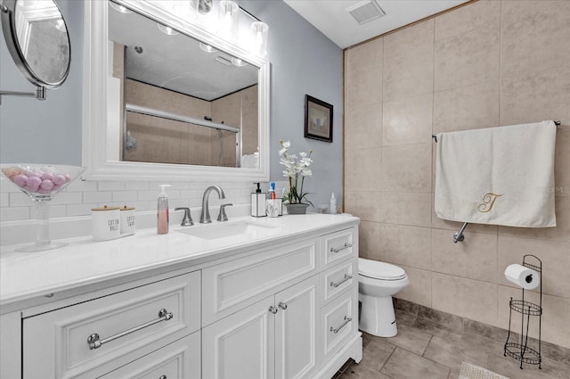 bathroom featuring toilet, vanity, tile walls, backsplash, and a shower with door