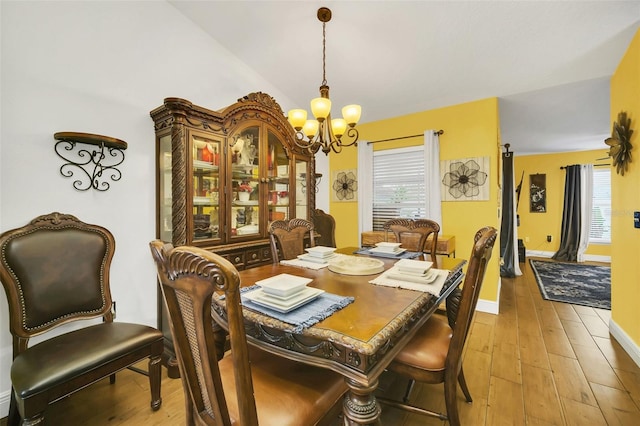 dining space with a notable chandelier, light wood-type flooring, and vaulted ceiling