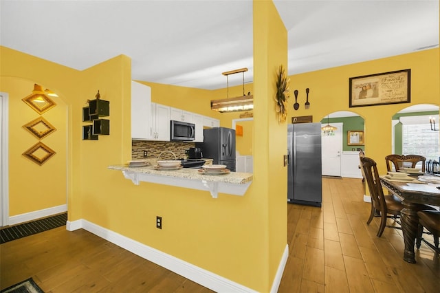 kitchen featuring a kitchen breakfast bar, stainless steel appliances, hardwood / wood-style floors, decorative light fixtures, and white cabinetry