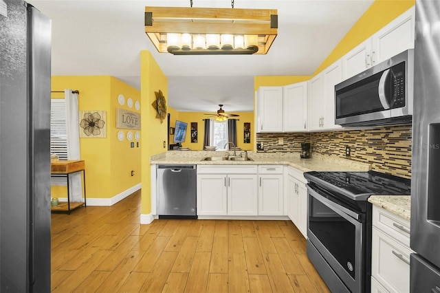 kitchen featuring light stone counters, appliances with stainless steel finishes, white cabinetry, light hardwood / wood-style floors, and sink