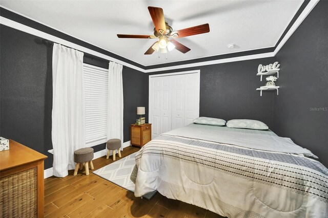 bedroom with a closet, ornamental molding, wood-type flooring, and ceiling fan