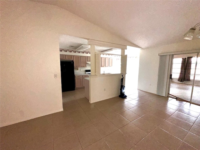 interior space with black refrigerator, lofted ceiling, and light tile patterned floors