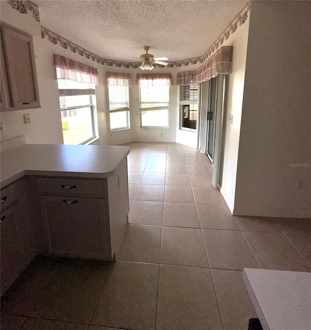 kitchen with a textured ceiling, kitchen peninsula, ceiling fan, and light tile patterned flooring