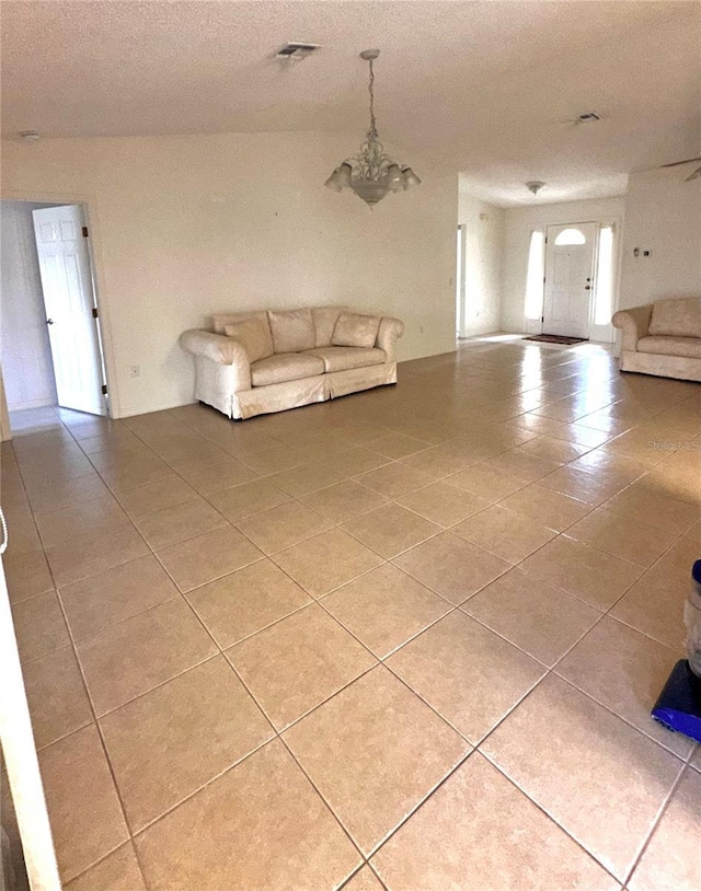 unfurnished living room featuring a notable chandelier, lofted ceiling, and tile patterned floors