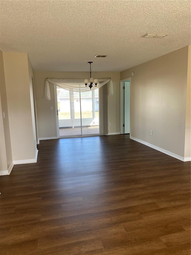 empty room featuring dark wood-type flooring, an inviting chandelier, and a textured ceiling