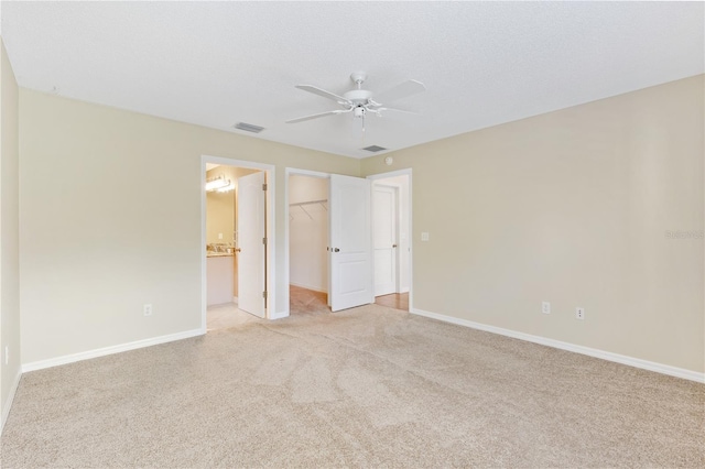 unfurnished bedroom featuring ceiling fan, a spacious closet, ensuite bathroom, light colored carpet, and a closet