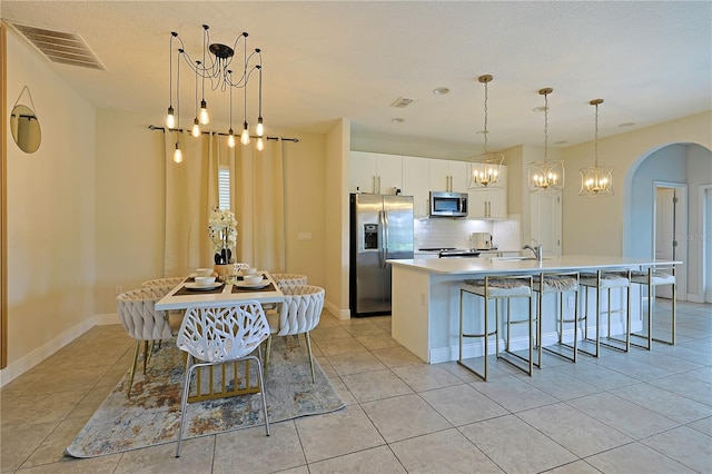 kitchen featuring white cabinets, a center island with sink, backsplash, appliances with stainless steel finishes, and a kitchen breakfast bar