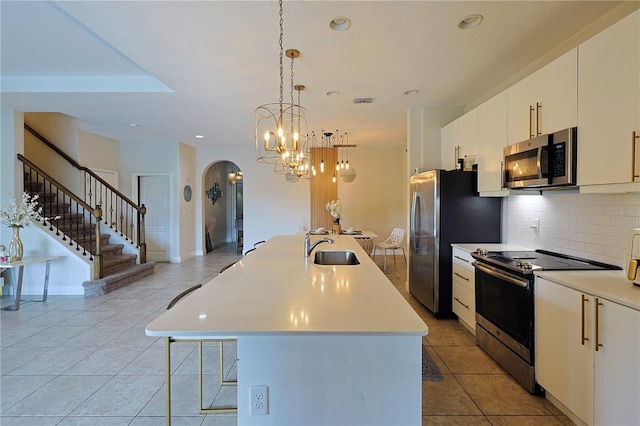 kitchen featuring white cabinets, hanging light fixtures, a center island with sink, sink, and stainless steel appliances