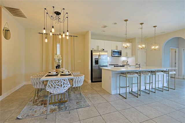 kitchen with white cabinets, tasteful backsplash, a center island with sink, appliances with stainless steel finishes, and a kitchen bar