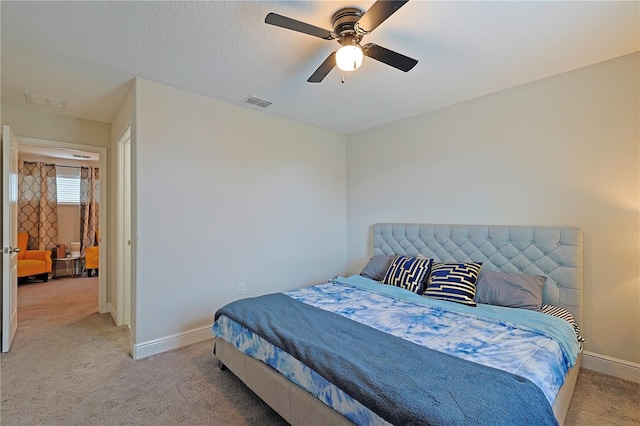 bedroom featuring a textured ceiling, light colored carpet, and ceiling fan