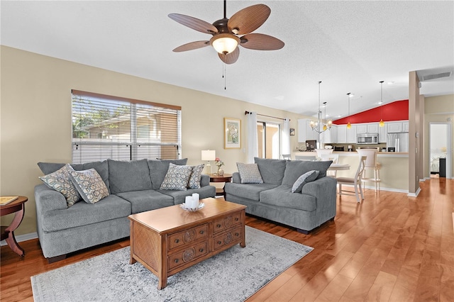 living room featuring a textured ceiling, wood-type flooring, lofted ceiling, and ceiling fan with notable chandelier