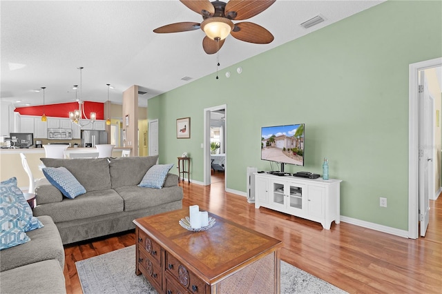 living room featuring vaulted ceiling, light hardwood / wood-style flooring, a textured ceiling, and ceiling fan with notable chandelier