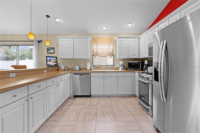 kitchen featuring appliances with stainless steel finishes, kitchen peninsula, white cabinetry, and decorative light fixtures