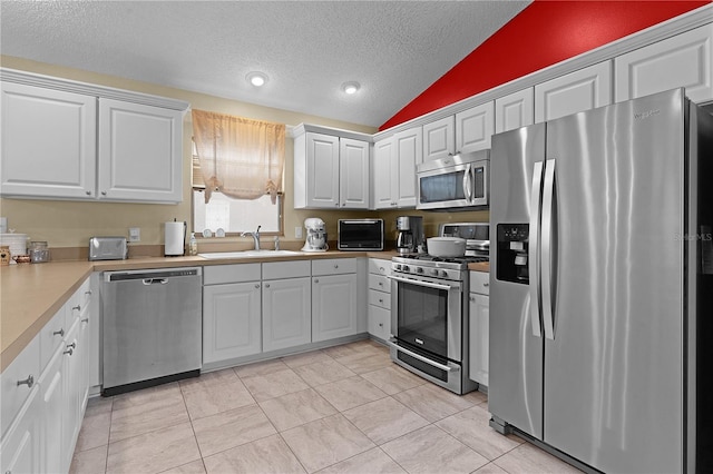 kitchen featuring appliances with stainless steel finishes, sink, a textured ceiling, white cabinetry, and lofted ceiling