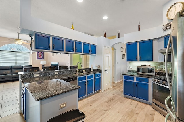 kitchen with light wood-type flooring, stainless steel appliances, sink, blue cabinetry, and dark stone countertops