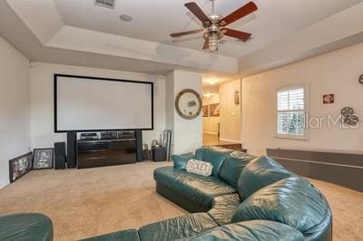 cinema with ceiling fan, a raised ceiling, and carpet