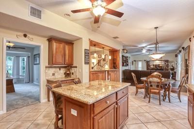 kitchen featuring a kitchen island, backsplash, light stone counters, light tile patterned floors, and pendant lighting