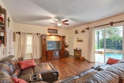 living room with a textured ceiling, ceiling fan, and dark hardwood / wood-style flooring