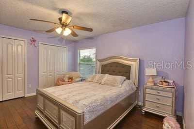 bedroom with a textured ceiling, dark wood-type flooring, two closets, and ceiling fan