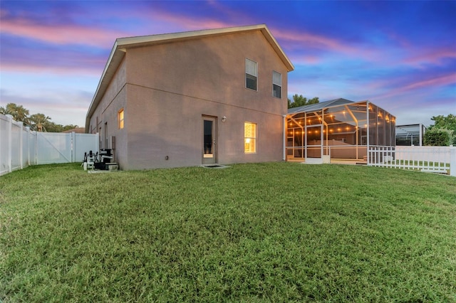 back house at dusk featuring a yard and glass enclosure