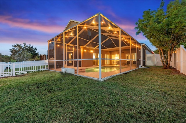 back house at dusk featuring a yard, a patio area, and a lanai