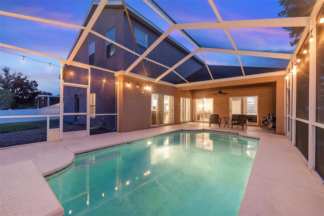 pool at dusk with a patio area, ceiling fan, and glass enclosure