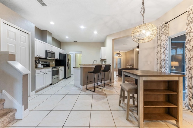 kitchen with appliances with stainless steel finishes, ceiling fan with notable chandelier, decorative light fixtures, white cabinets, and a breakfast bar