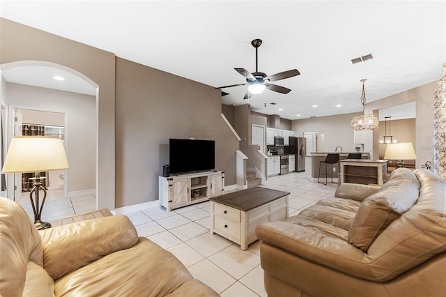 tiled living room with ceiling fan with notable chandelier