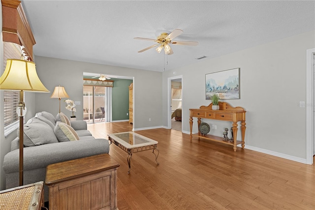 living room featuring light hardwood / wood-style floors, ceiling fan, and a textured ceiling