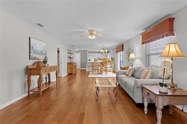 living room with light hardwood / wood-style floors, ceiling fan with notable chandelier, and a textured ceiling