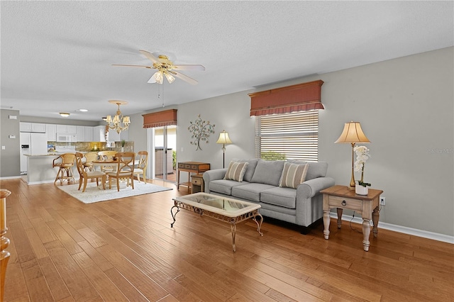 living room with ceiling fan with notable chandelier, light hardwood / wood-style flooring, and a textured ceiling