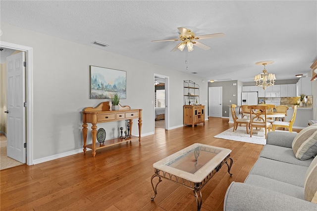 living room featuring hardwood / wood-style floors, ceiling fan with notable chandelier, and a textured ceiling