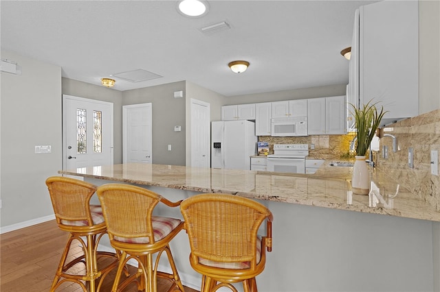 kitchen with white cabinetry, kitchen peninsula, backsplash, white appliances, and light hardwood / wood-style flooring