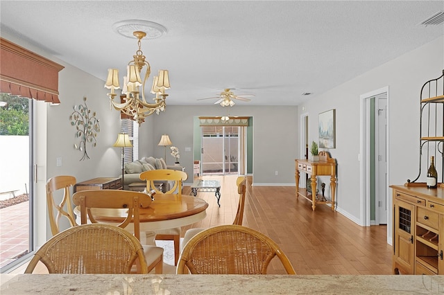 dining area with light wood-type flooring, a textured ceiling, and ceiling fan with notable chandelier