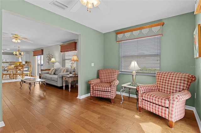 sitting room with ceiling fan with notable chandelier and wood-type flooring