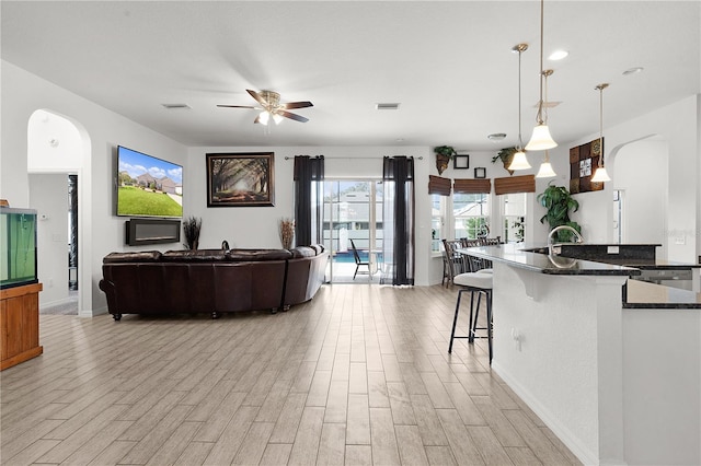 kitchen with ceiling fan, a kitchen bar, light hardwood / wood-style flooring, dark stone countertops, and pendant lighting