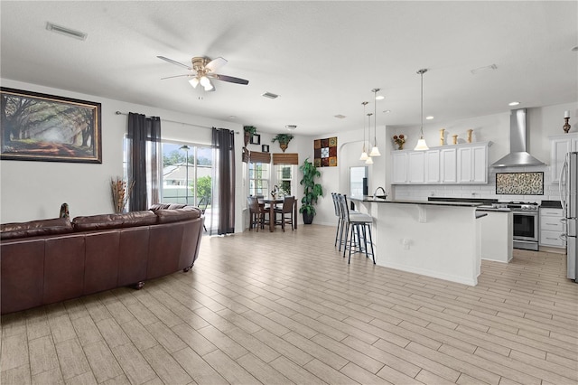 kitchen featuring wall chimney exhaust hood, a kitchen bar, pendant lighting, white cabinetry, and appliances with stainless steel finishes