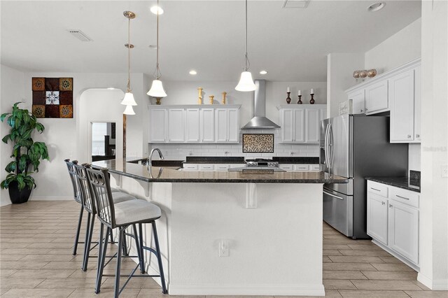 kitchen featuring wall chimney exhaust hood, stainless steel fridge with ice dispenser, white cabinetry, and a center island with sink