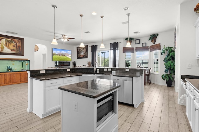 kitchen featuring appliances with stainless steel finishes, a center island, dark stone counters, decorative light fixtures, and white cabinets