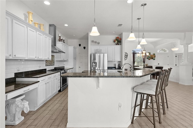 kitchen featuring a large island, hanging light fixtures, light wood-type flooring, wall chimney exhaust hood, and stainless steel appliances