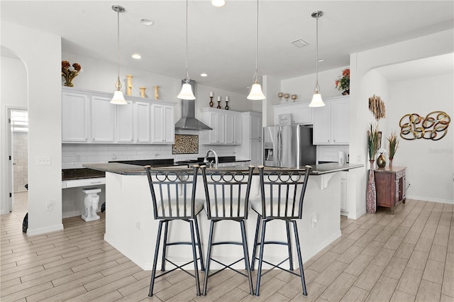 kitchen with a kitchen island with sink, stainless steel refrigerator with ice dispenser, white cabinets, and pendant lighting