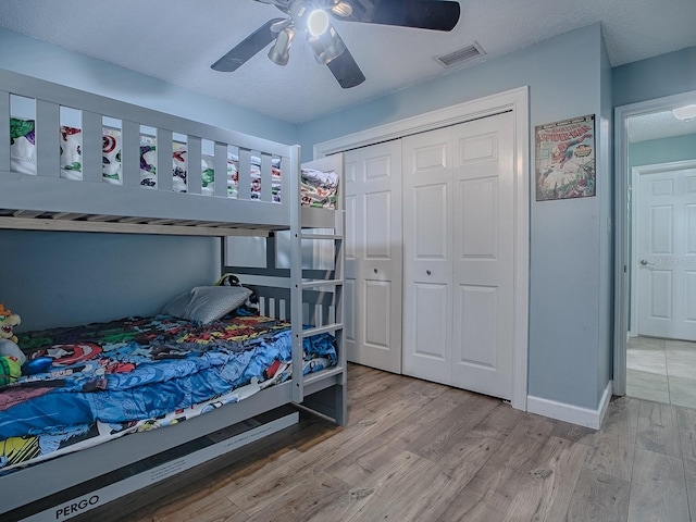 bedroom featuring a closet, light hardwood / wood-style floors, a textured ceiling, and ceiling fan