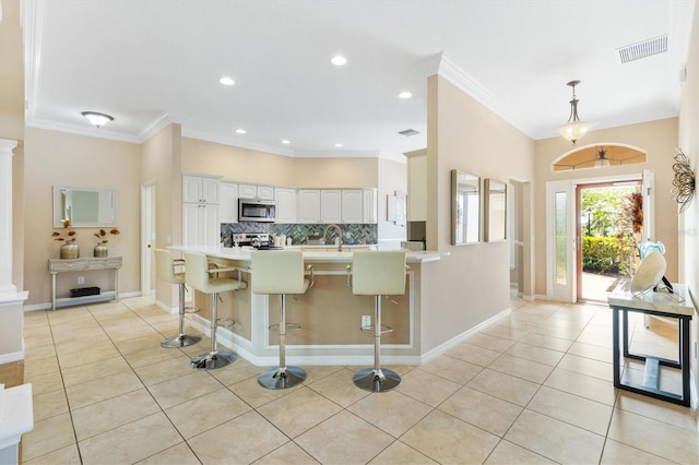 kitchen featuring kitchen peninsula, a kitchen breakfast bar, stainless steel appliances, crown molding, and white cabinets