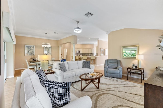 living room featuring decorative columns, vaulted ceiling, crown molding, an inviting chandelier, and light hardwood / wood-style floors